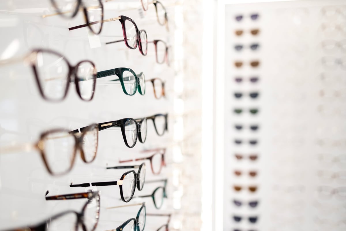 Large group of eyeglasses frames standing on the shelves in optician store.