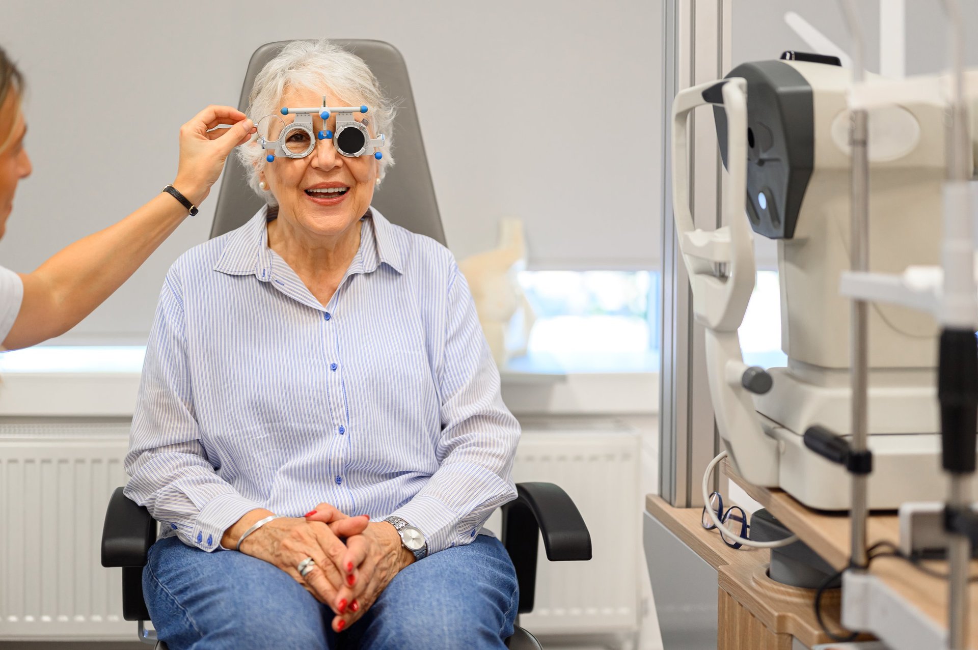 Female doctor adjusting phoropter lenses while happy senior woman undergoes vision test at ophthalmology clinic
