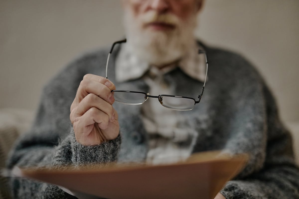 Senior Caucasian man holding eyeglasses while reading document, suggesting concentration and engagement with paperwork